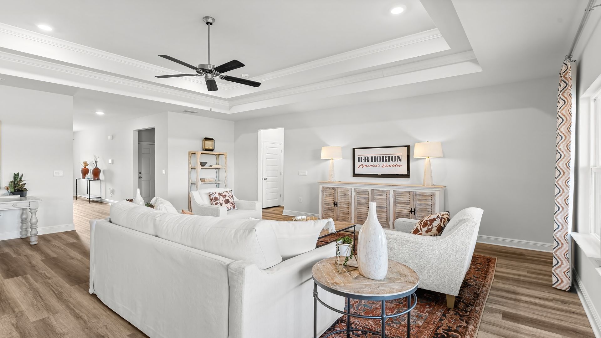 Open living room with EVP flooring and tray ceilings and ceiling fan.