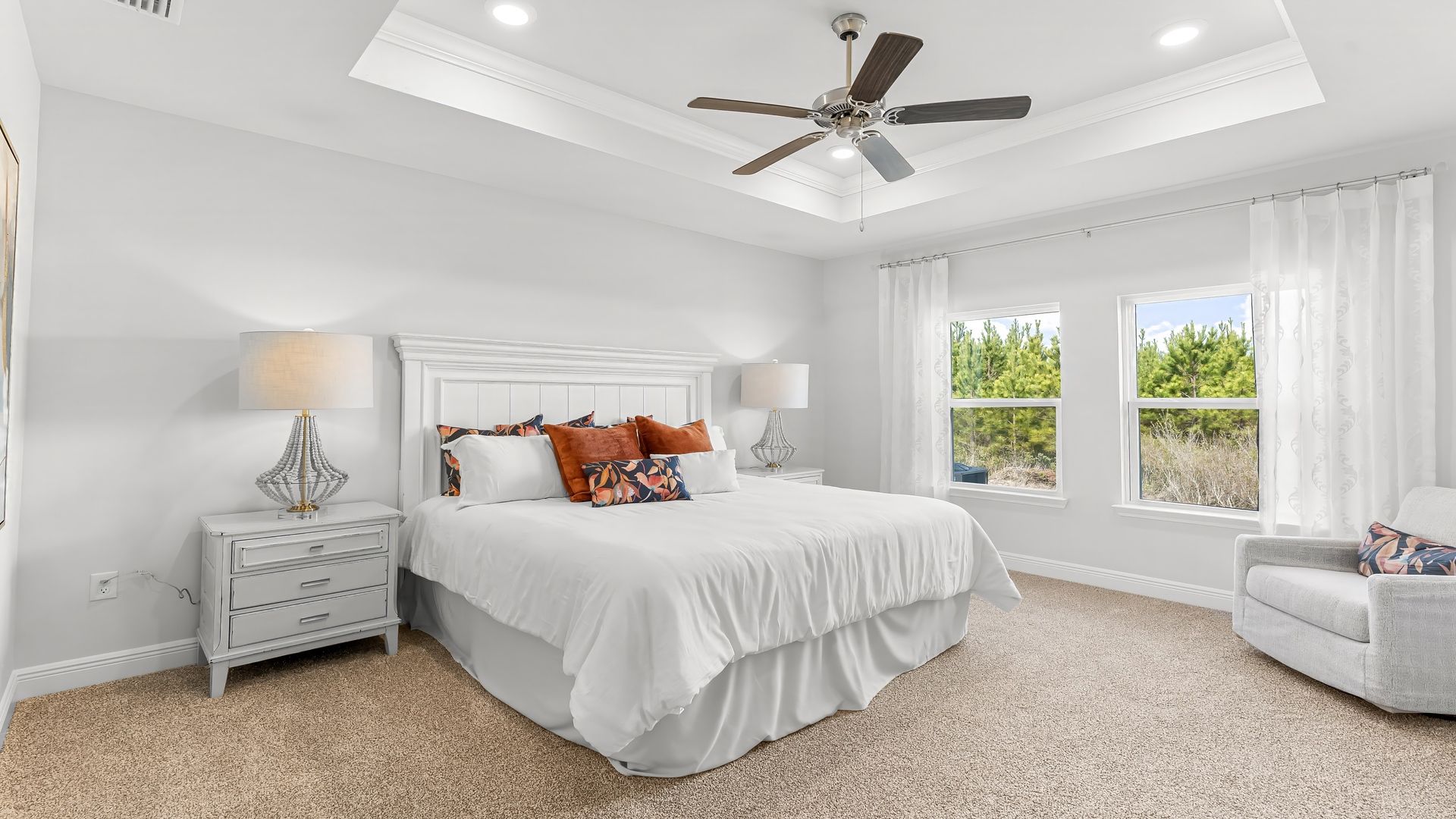 Primary bedroom with carpet floors and ceiling fan and tray ceilings and two windows.