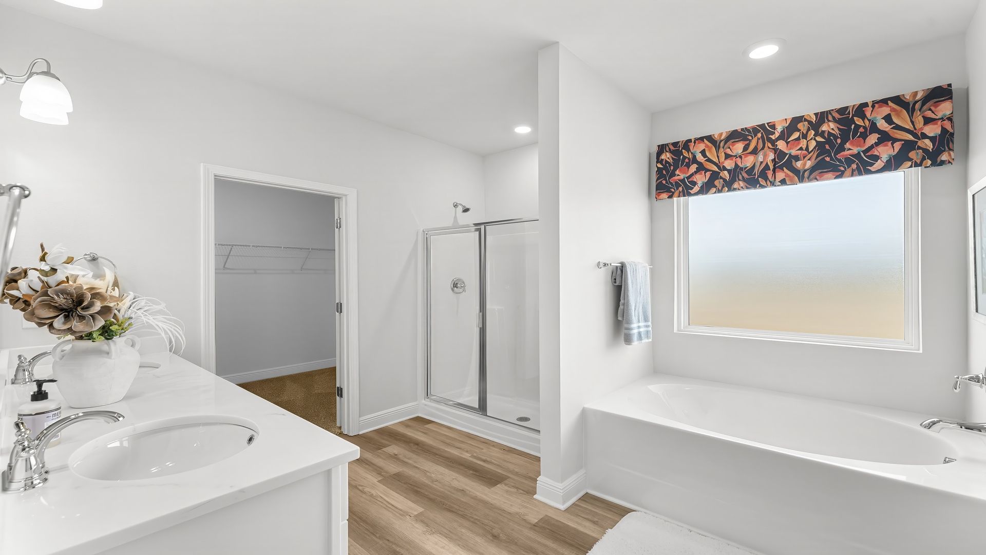 Primary bathroom with EVP flooring and white cabinets and double vanity with quartz countertops and walk-in shower with glass doors and tub with window and closet.