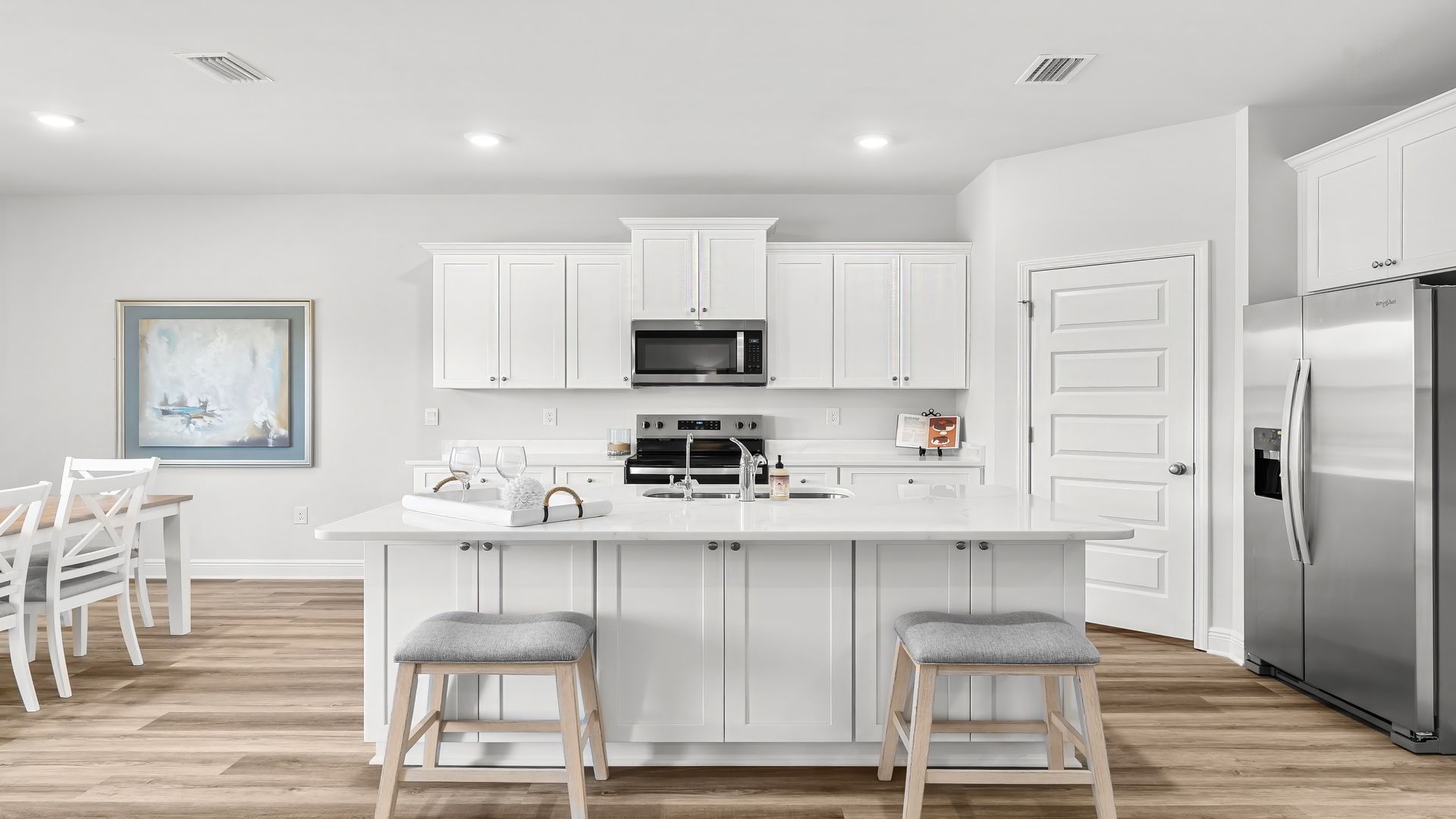 Kitchen with island with white cabinets and quartz countertops and pantry and stainless-steel appliances.