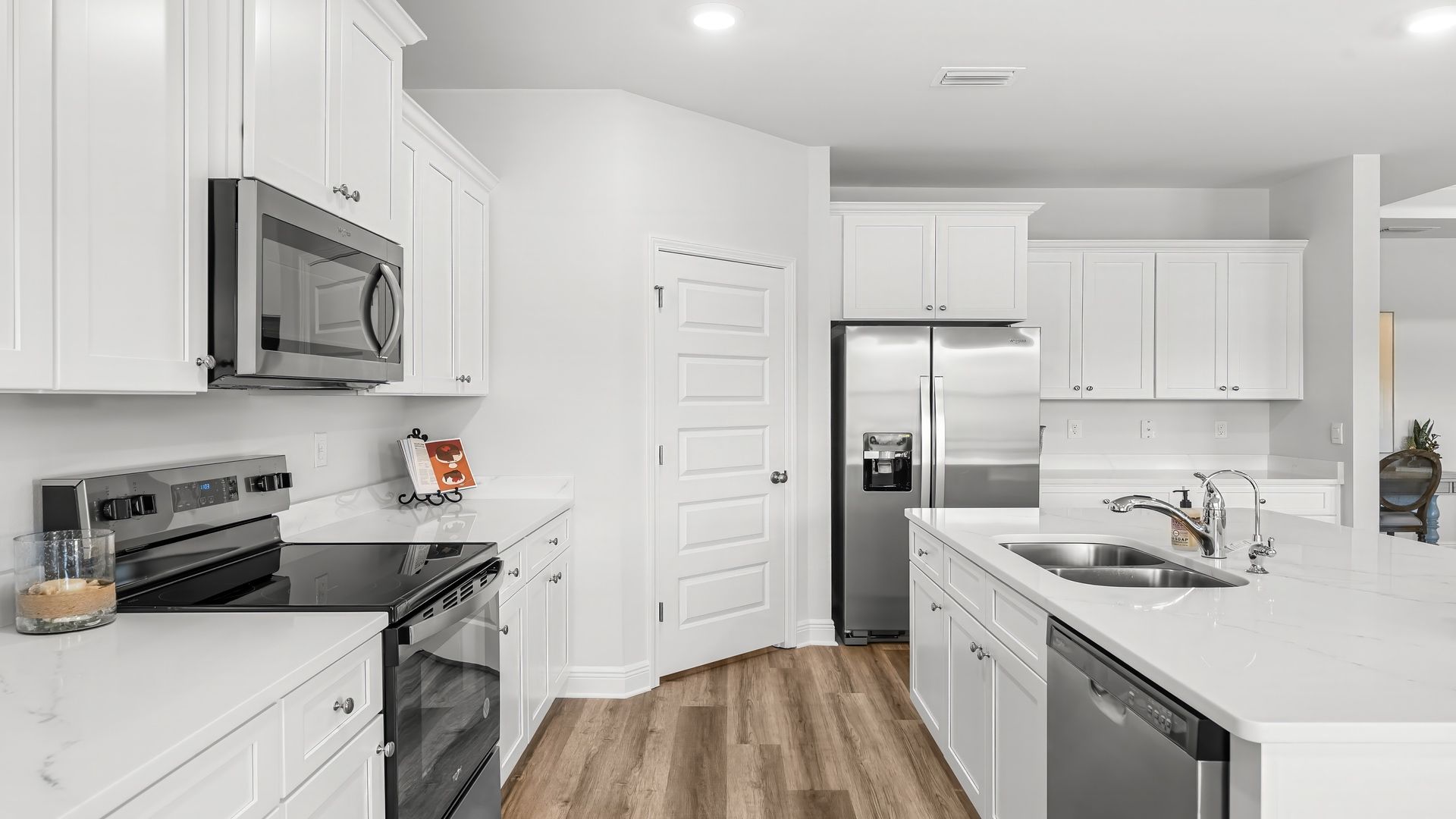 Kitchen with island with white cabinets and quartz countertops and pantry and stainless-steel appliances.