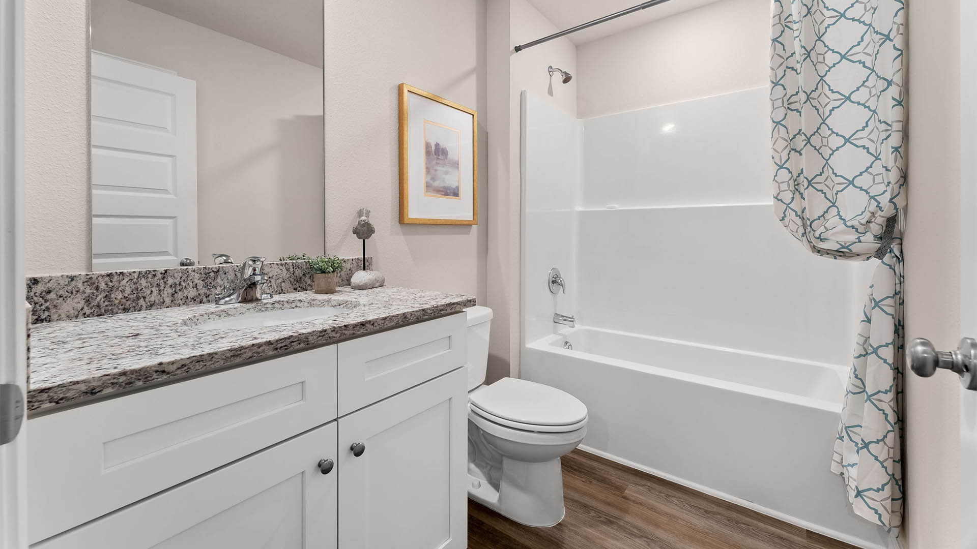 Bathroom with granite countertops and white cabinets with single vanity and toilet and tub and shower combo.
