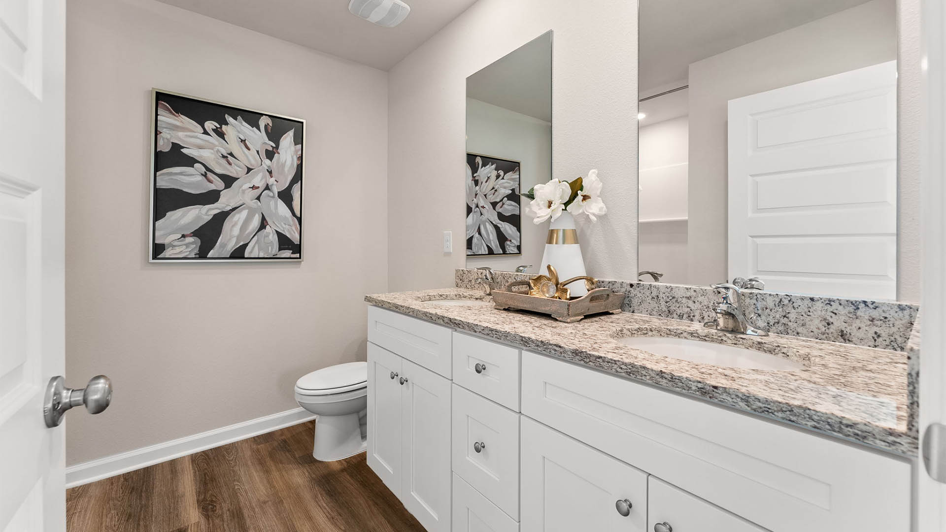Primary bathroom with EVP flooring and double vanity with granite countertops and white cabinets and toilet and shower.