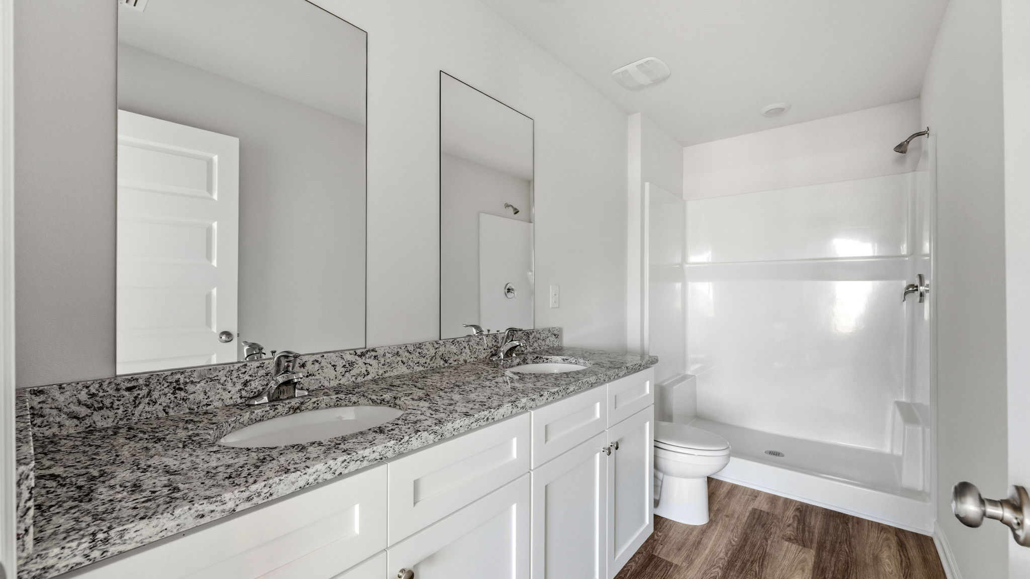 Primary bathroom with granite countertops and double vanity and toilet and shower.