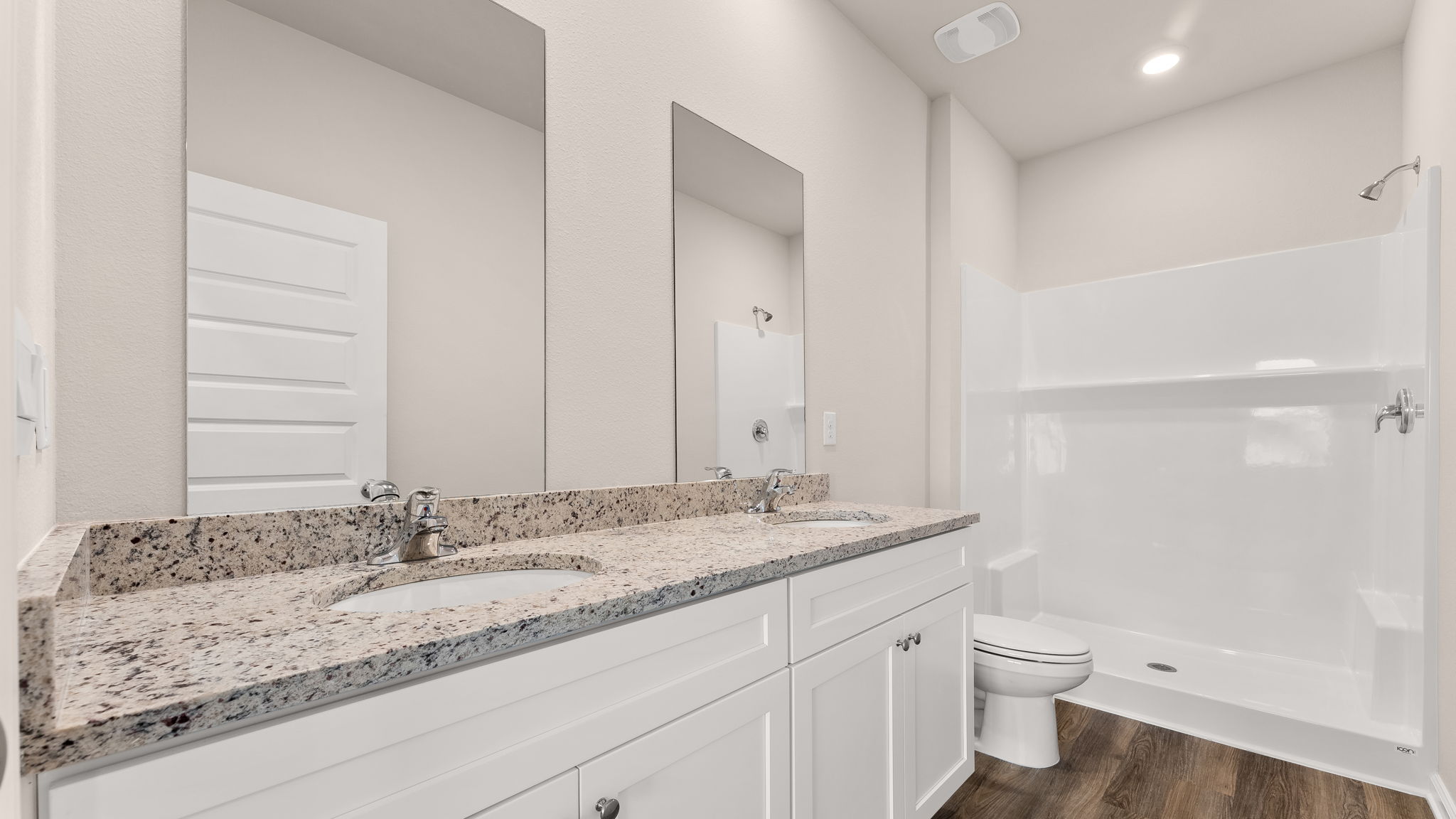 Primary bathroom with double vanity sinks and granite countertops with white cabinets and EVP flooring and shower and toilet.