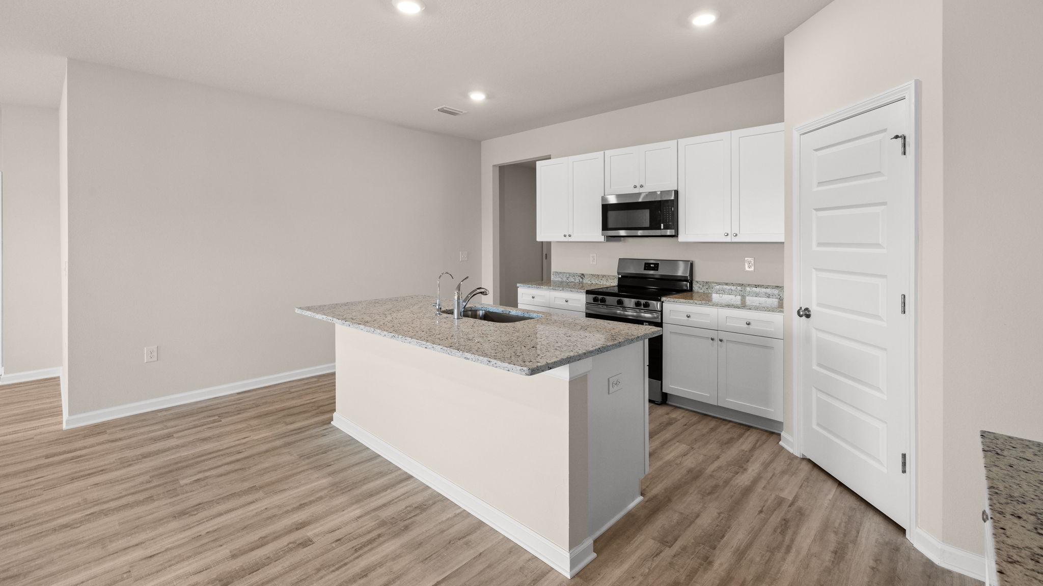 Kitchen with island and granite countertops with white cabinets and stainless-steel appliances.