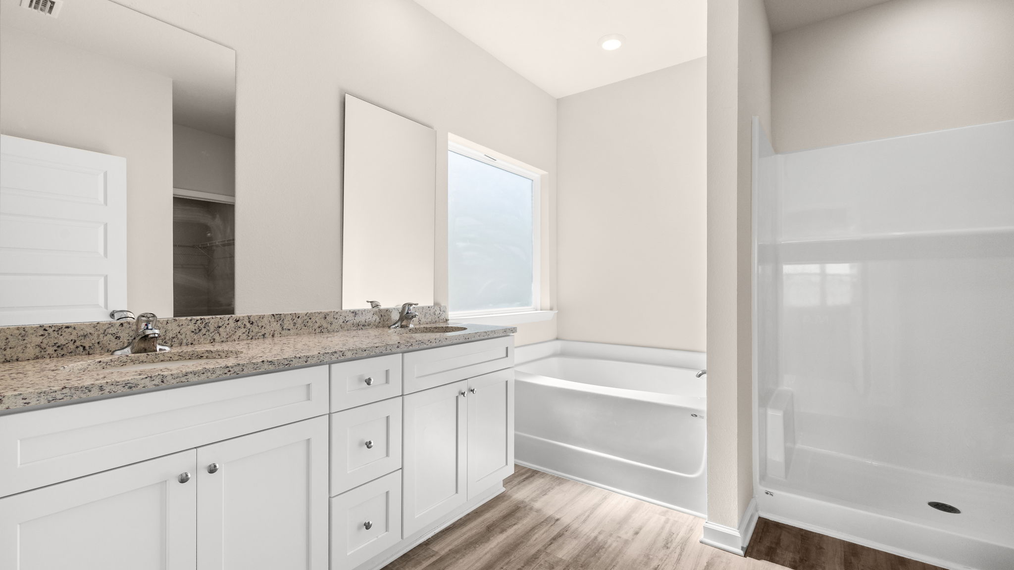 Primary bathroom with double vanity sink and granite countertops with white cabinets and EVP flooring and shower and toilet.