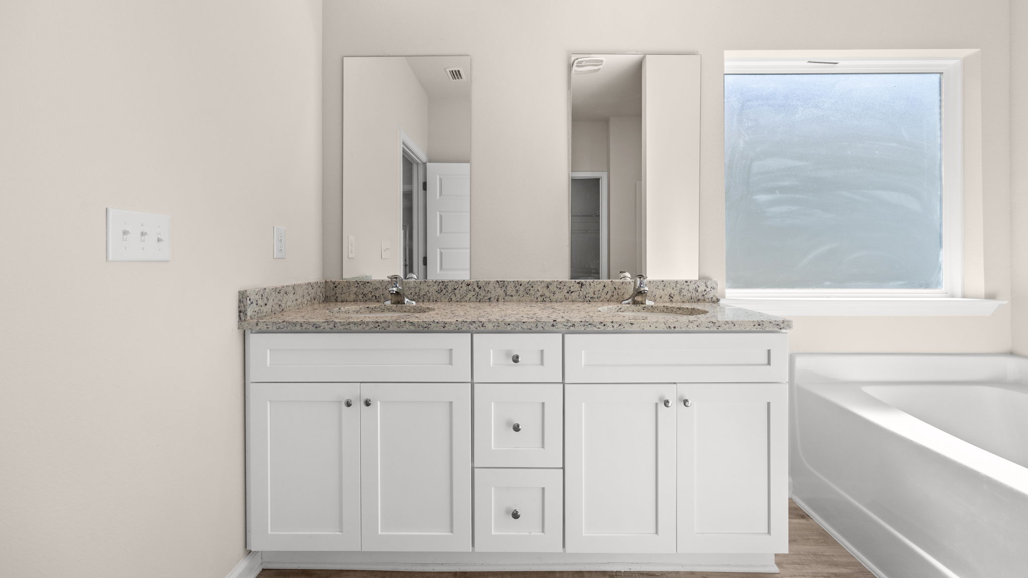 Primary bathroom with double vanity sink and granite countertops with white cabinets and EVP flooring and tub.