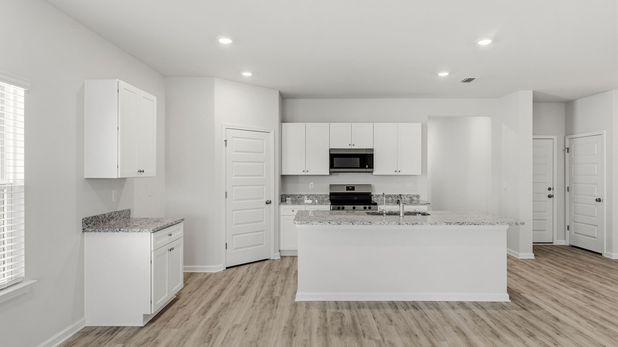 Kitchen with island and granite countertops with white cabinets and stainless-steel appliances.