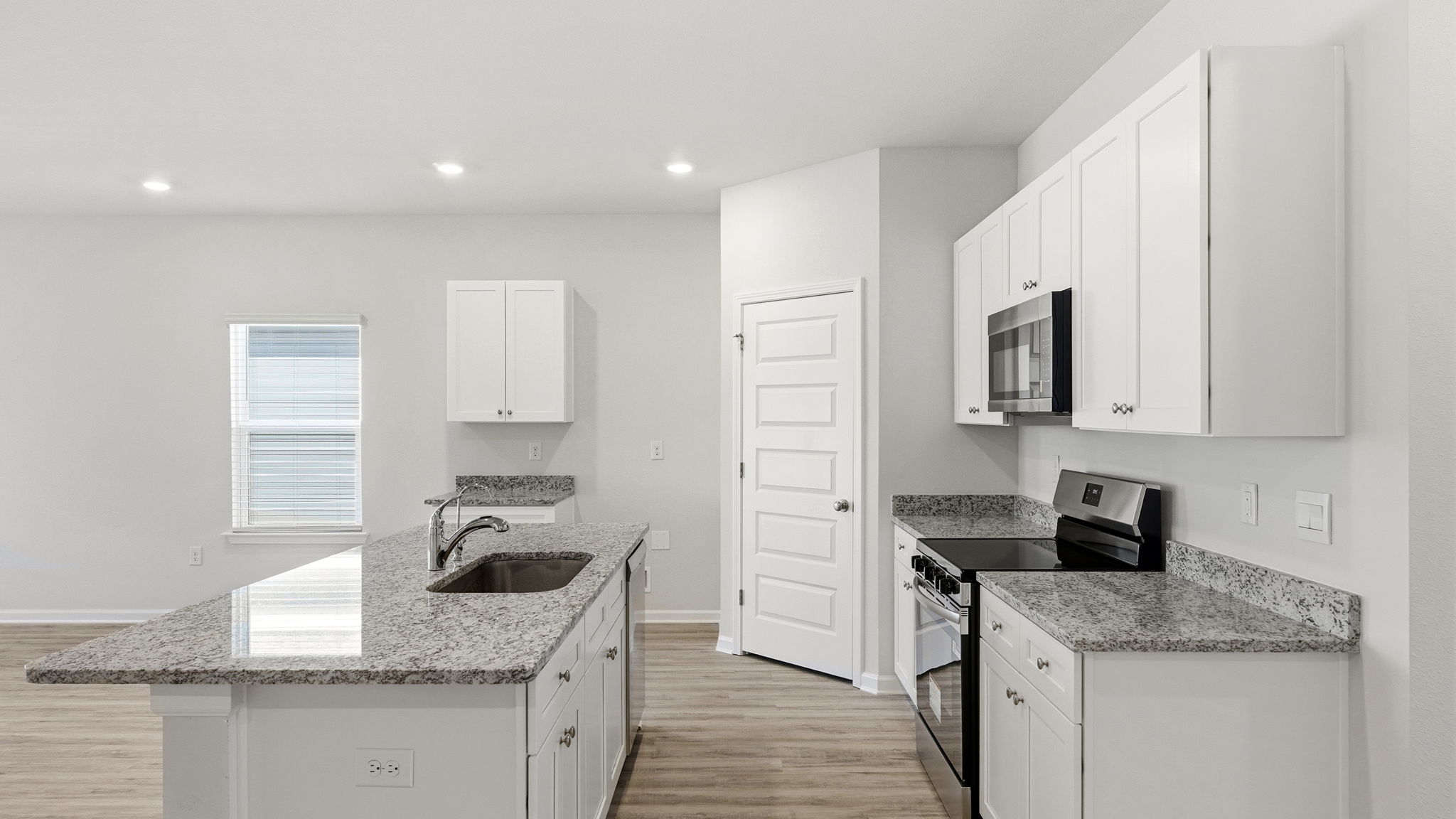 Kitchen with island and granite countertops with white cabinets and stainless-steel appliances.