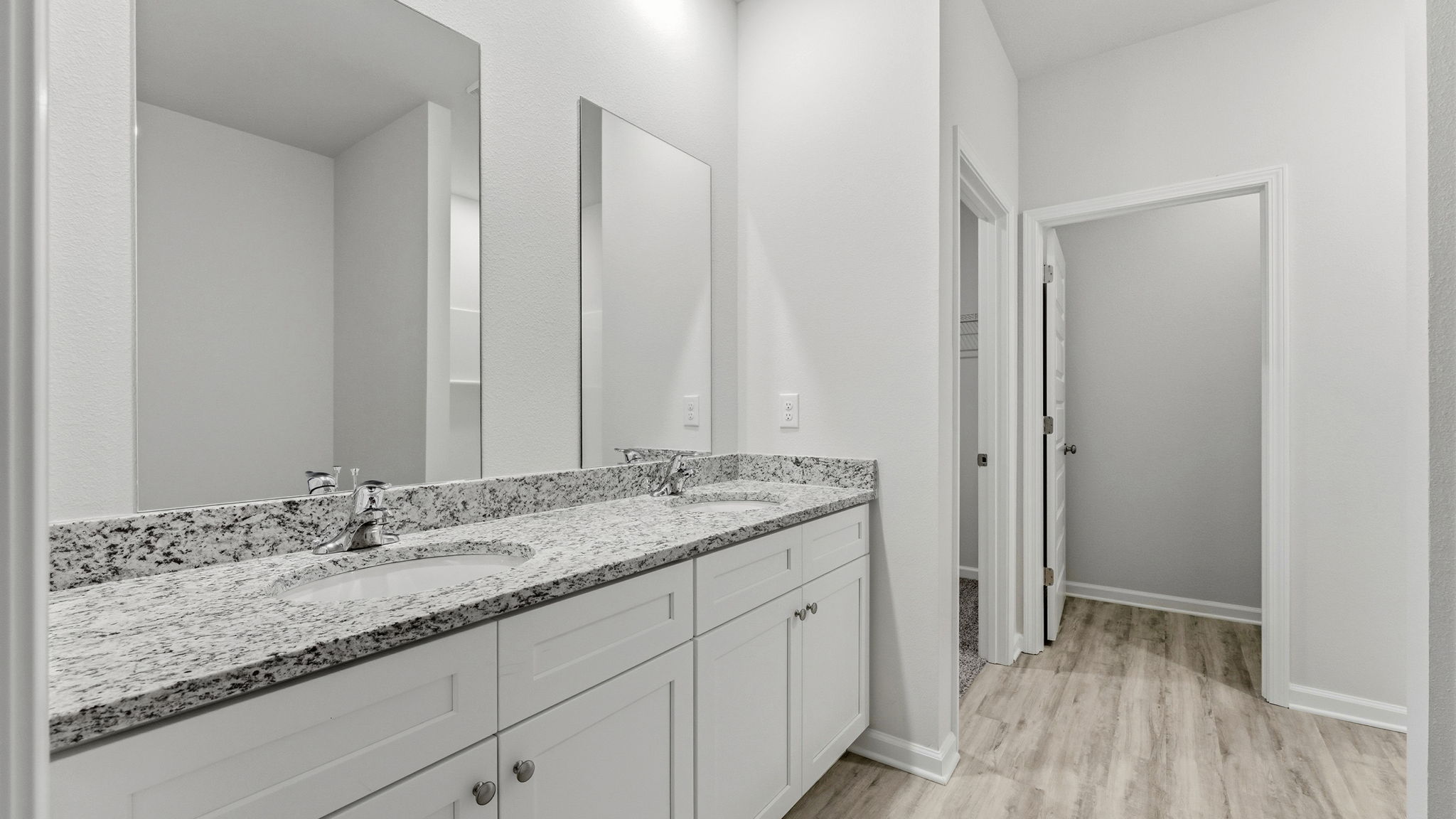 Primary bathroom with double vanity sinks and granite countertops with white cabinets and EVP flooring.