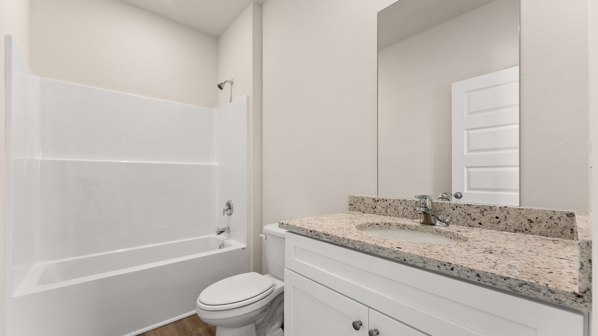 Bathroom with single vanity sink and granite countertops with white cabinets and EVP flooring and shower and toilet.