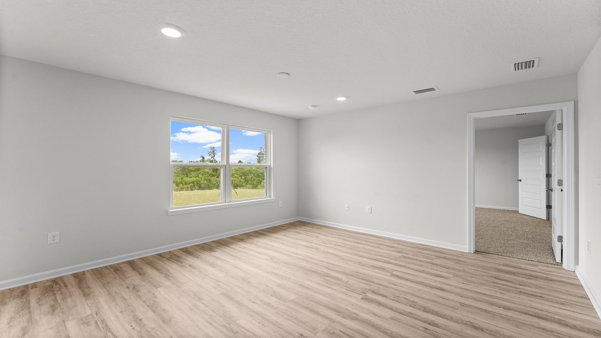 Open living room with EVP flooring and two windows and bedroom door.