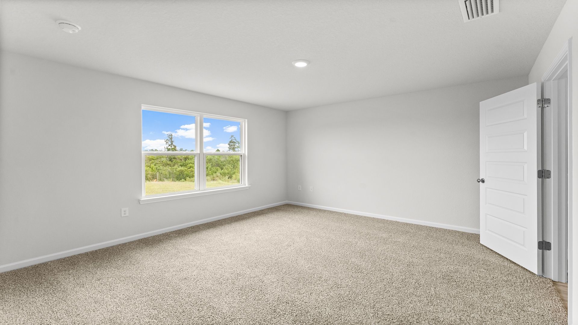 Primary bedroom with carpet flooring and two windows and bathroom door.