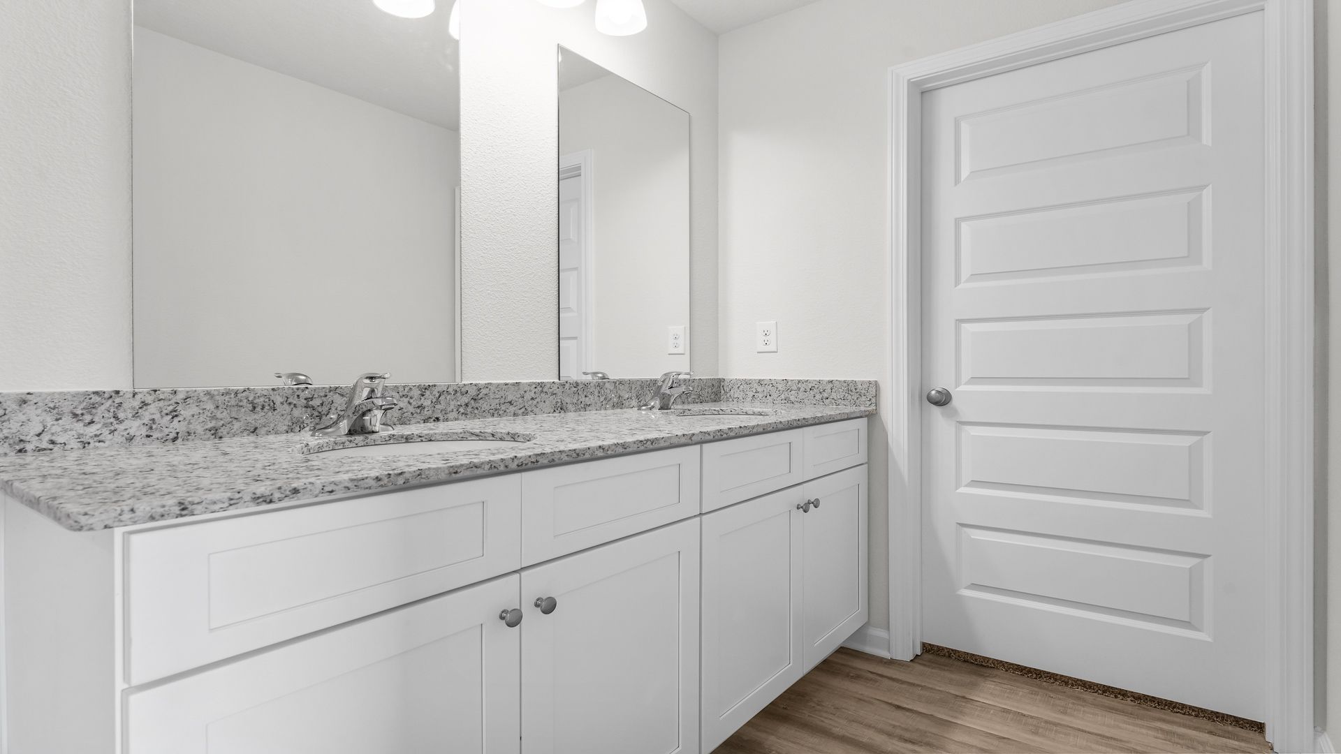 Primary bathroom with EVP flooring and white cabinets and double vanity and granite countertops.