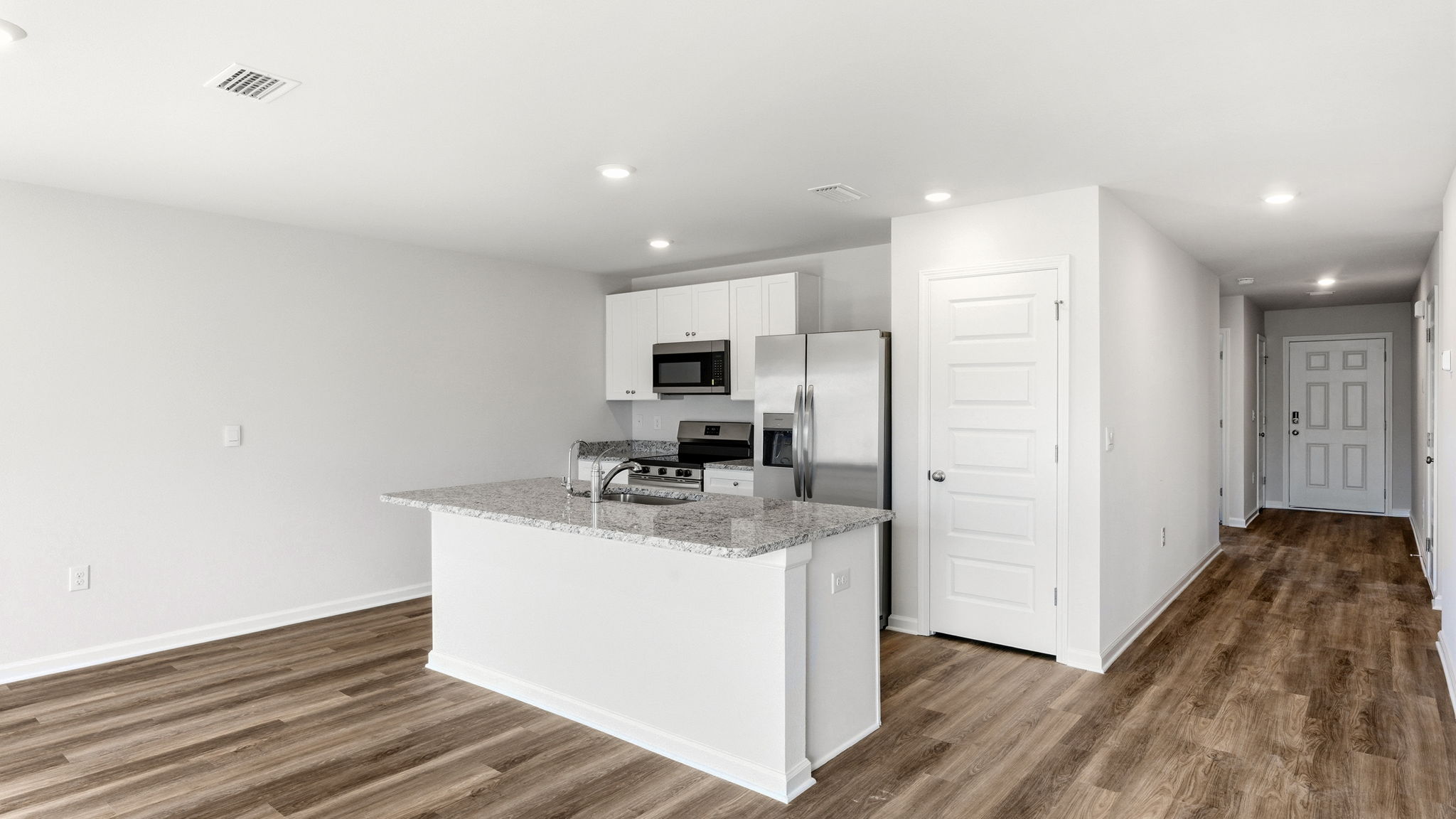 Kitchen island with granite countertops and stainless-steel appliances and living room with EVP flooring and pantry.