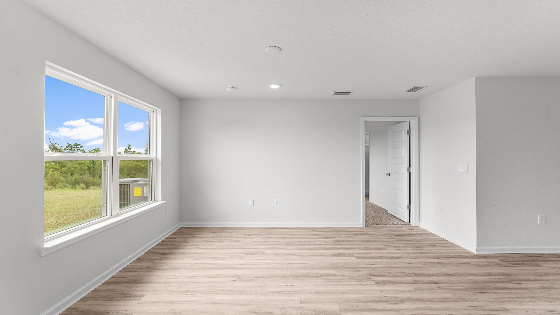 Open living room with EVP flooring and two windows and bedroom door.