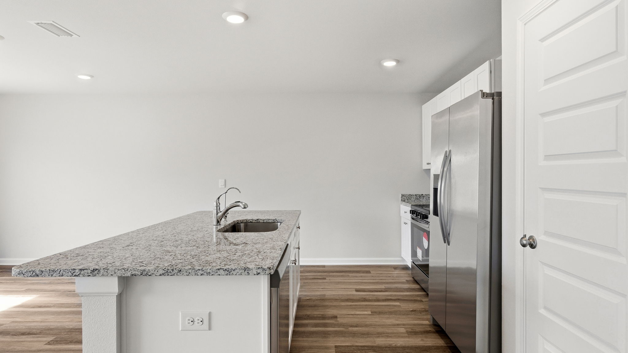Kitchen island with granite countertops and stainless-steel appliances and living room with EVP flooring and pantry.