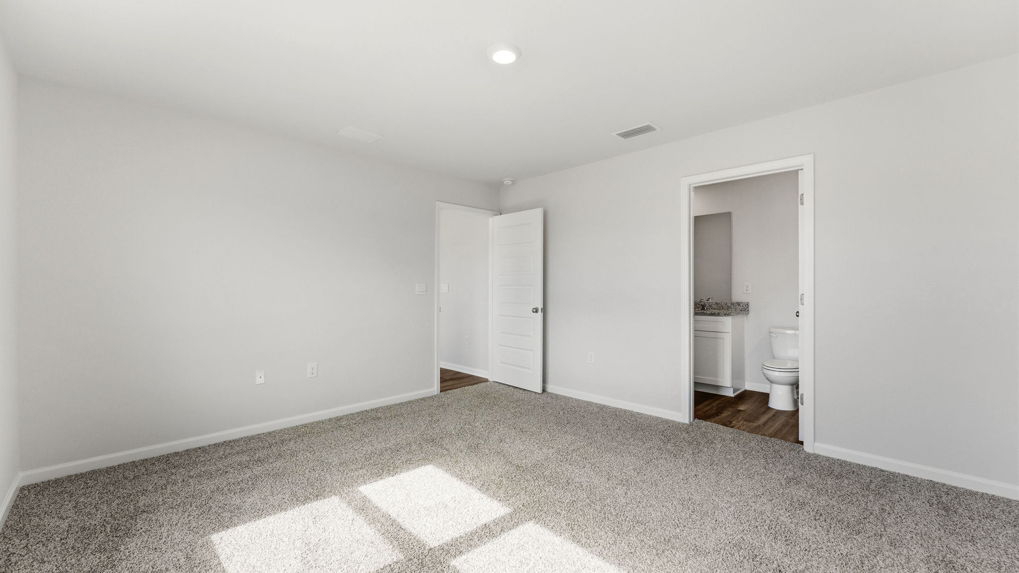 Primary bedroom with carpet flooring and bathroom entrance.