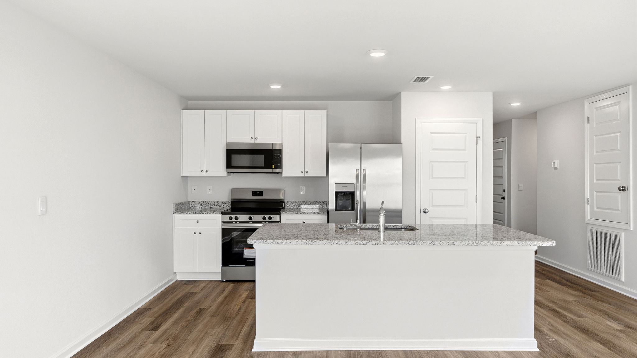 Kitchen island with granite countertops and stainless-steel appliances and living room with EVP flooring and pantry.