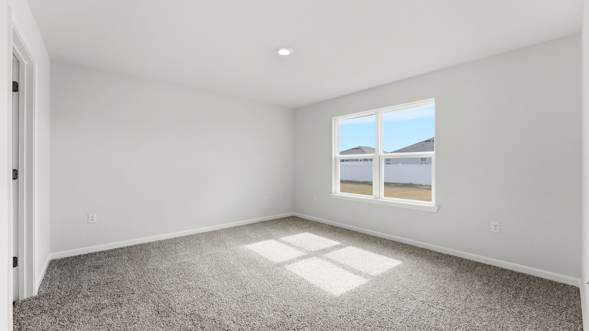 Primary bedroom with carpet flooring and two windows and bathroom entrance.
