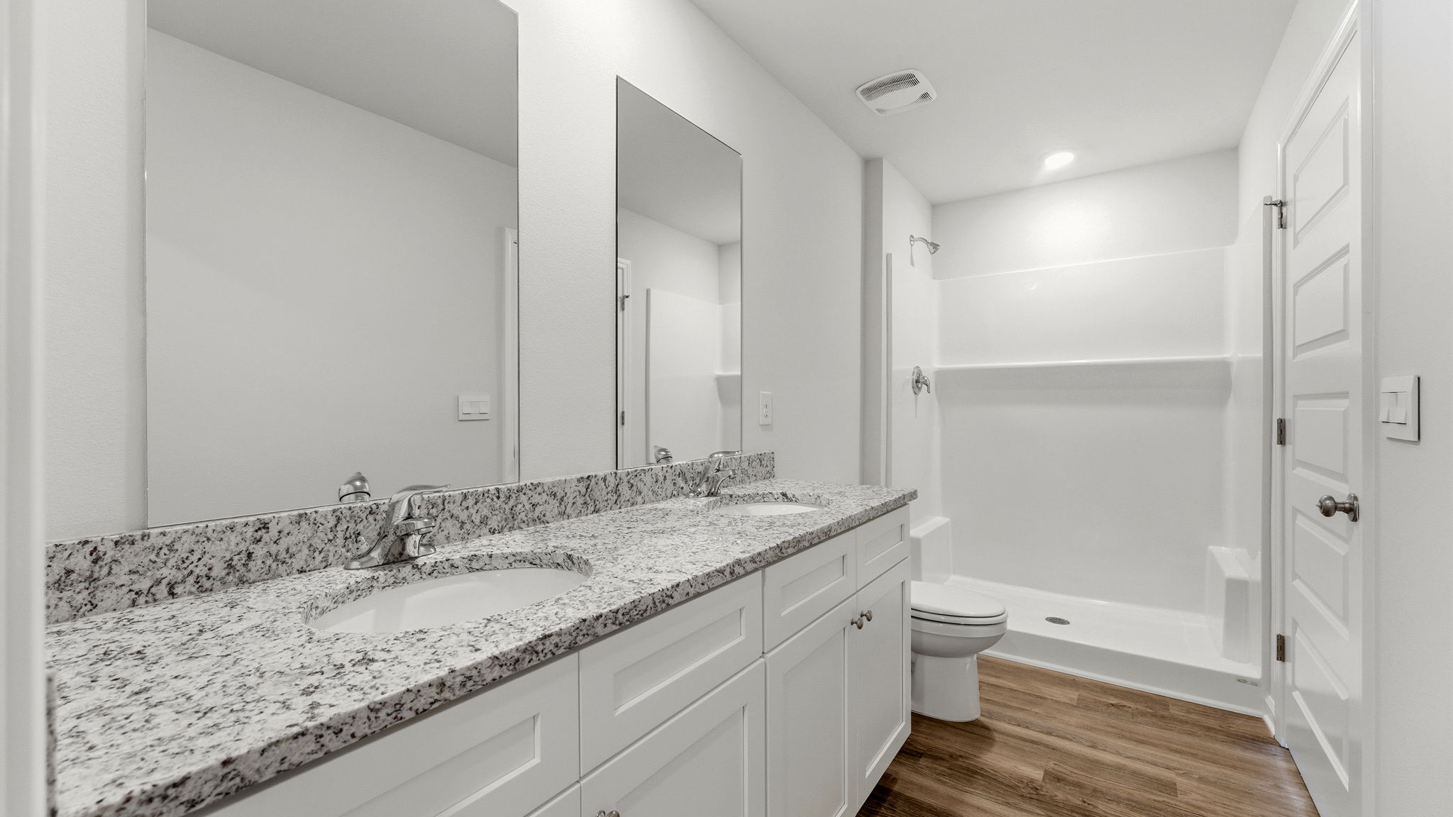 Primary bathroom with double vanity and granite countertops and toilet and shower.