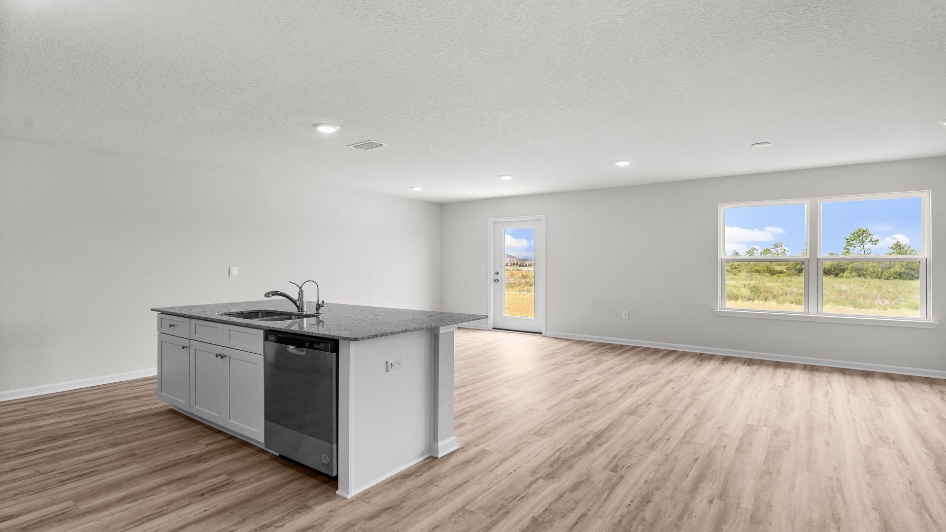 Kitchen island with granite countertops and stainless-steel appliances and living room with EVP flooring.