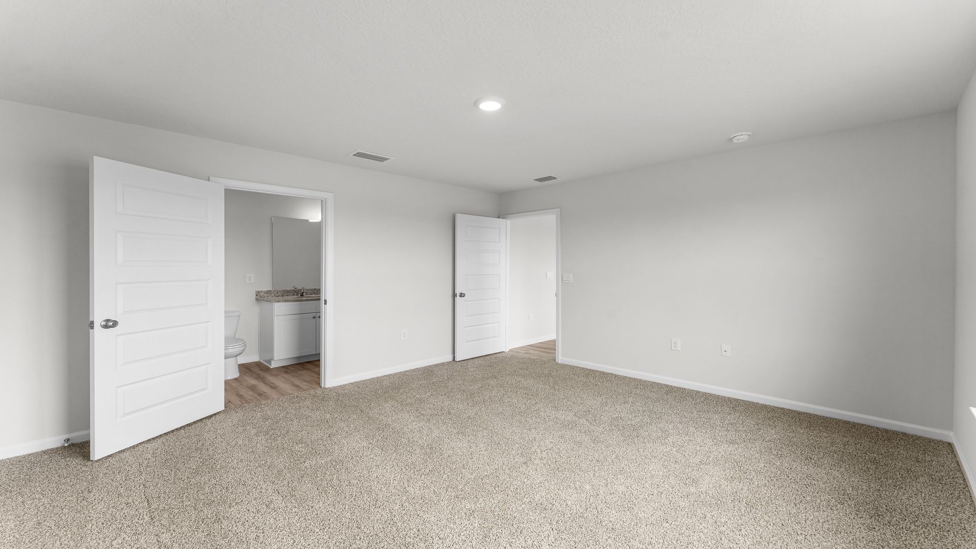 Primary bedroom with carpet flooring and bathroom door.
