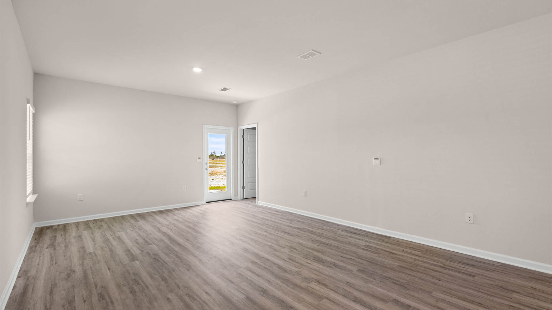 Open living room with EVP flooring and back door and bedroom entrance.