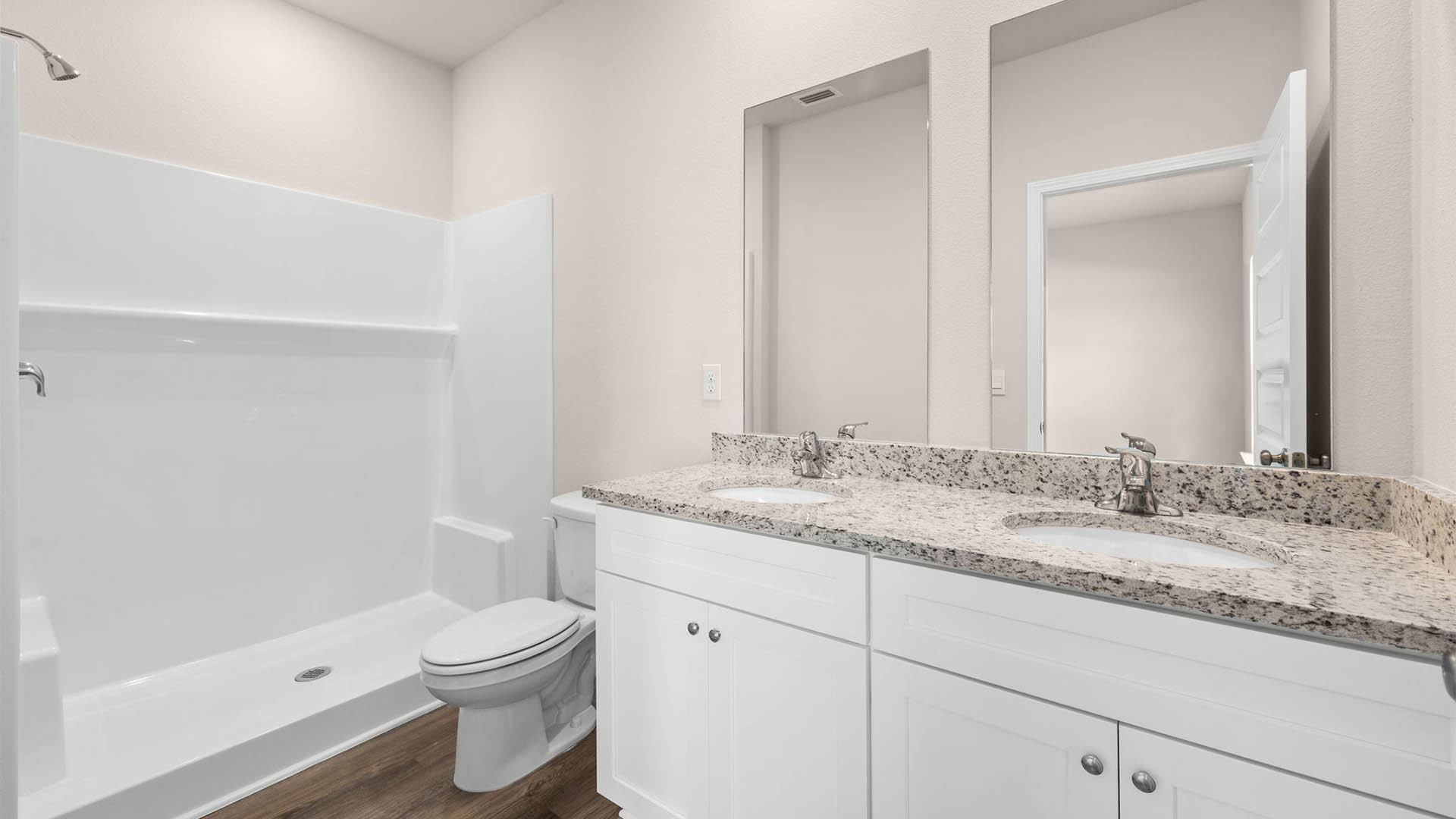 Primary bathroom with granite countertops and white cabinets and double vanity sinks and toilet and shower.