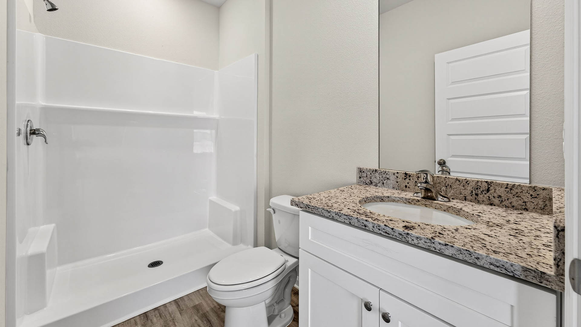 Primary bathroom with granite countertops and white cabinets and single vanity sinks and toilet and shower.