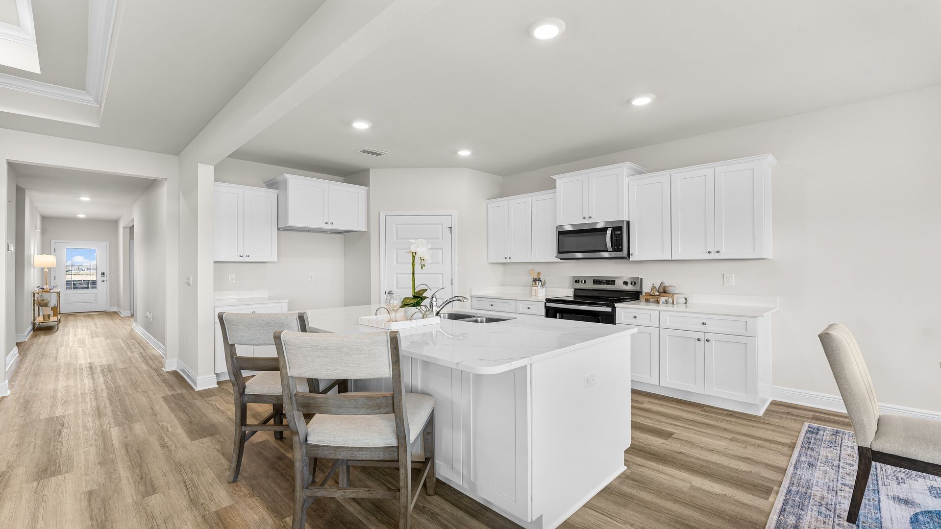 Open kitchen with island with quartz countertops and white cabinets and stainless-steel appliances and pantry.