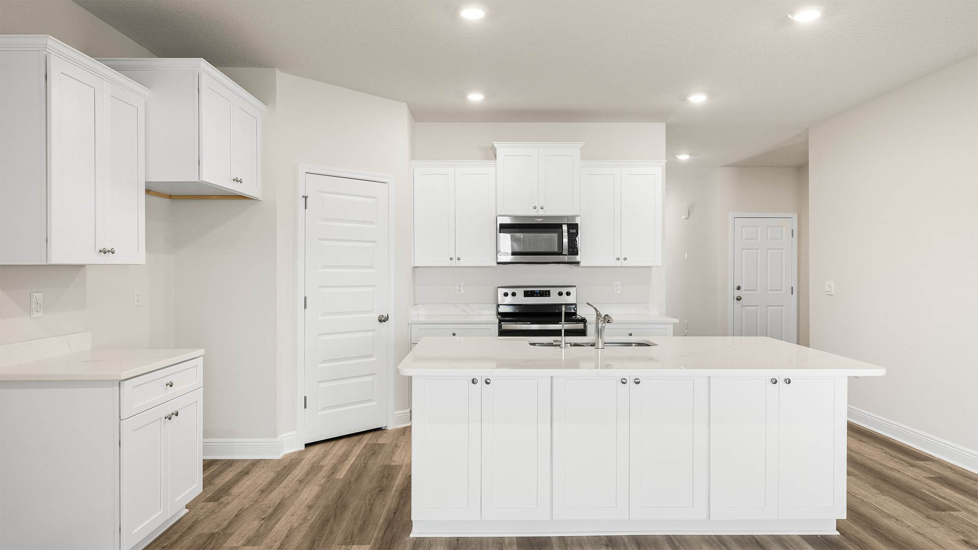 Kitchen with island and quartz countertops and white cabinets and stainless-steel appliances.