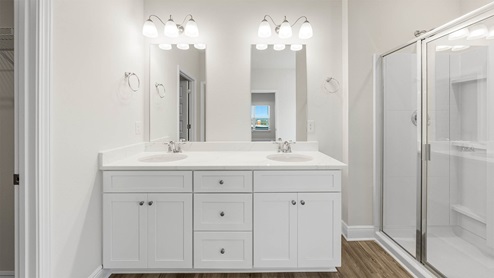 Primary bathroom with double vanity quartz countertops and shower with glass door and EVP flooring.