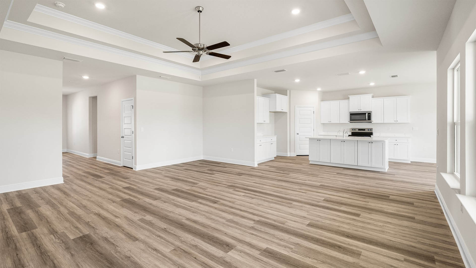 Open living room with EVP flooring and tray ceilings and ceiling fan and kitchen.