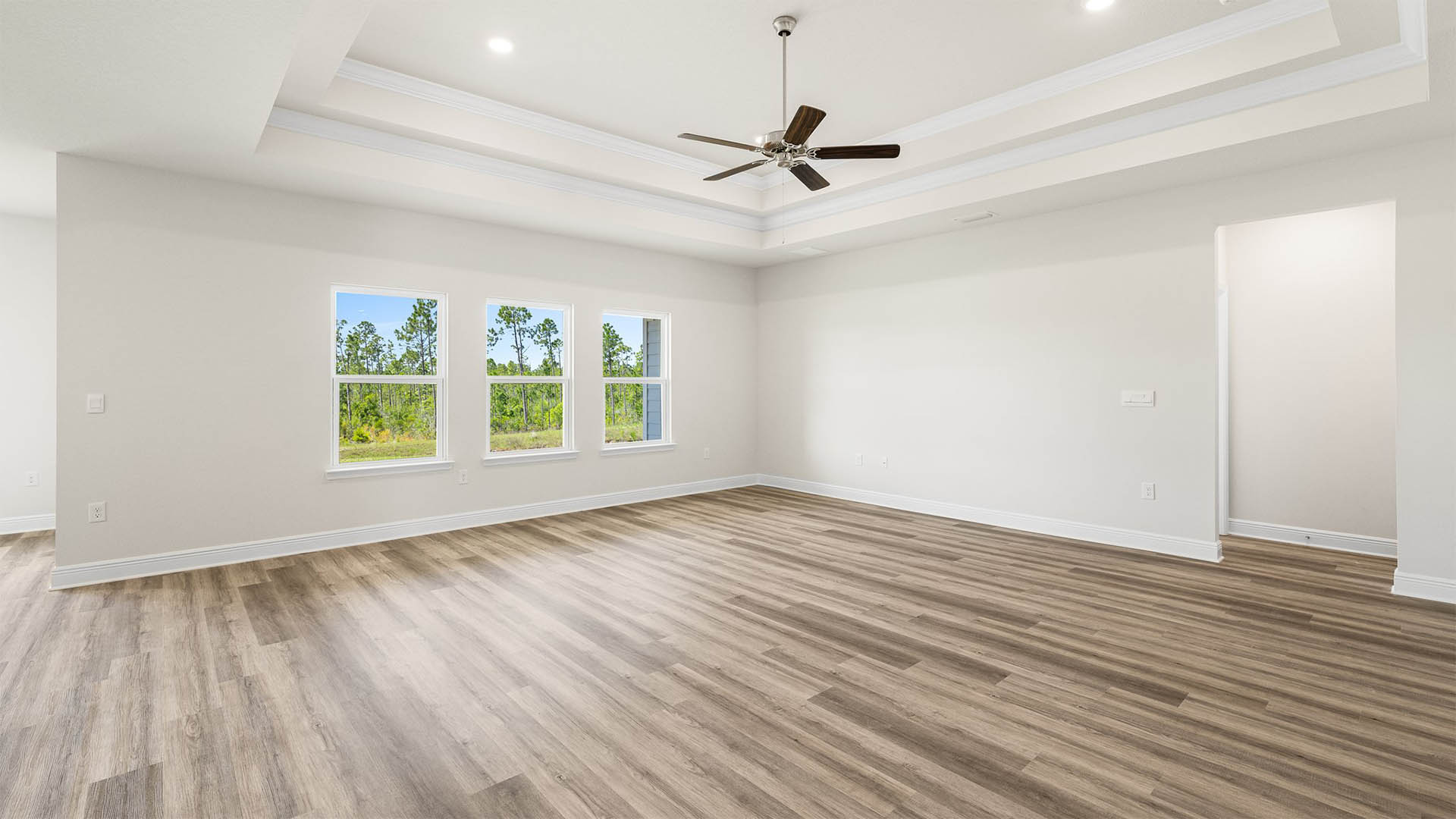 Open living room with EVP flooring and tray ceilings and ceiling fan and 3 windows.