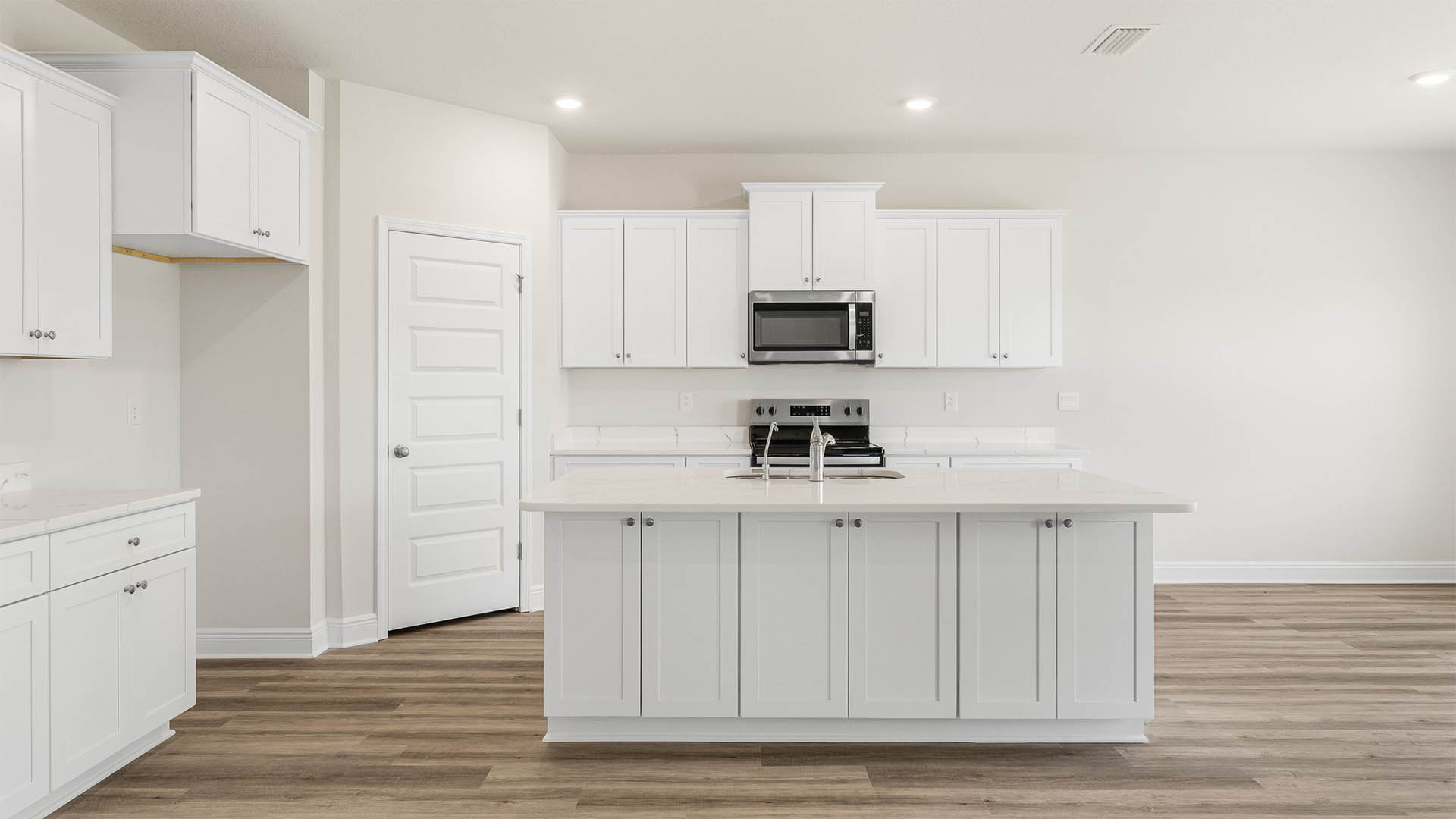 Open kitchen with island and quartz countertops and white cabinets and stainless-steel appliances.