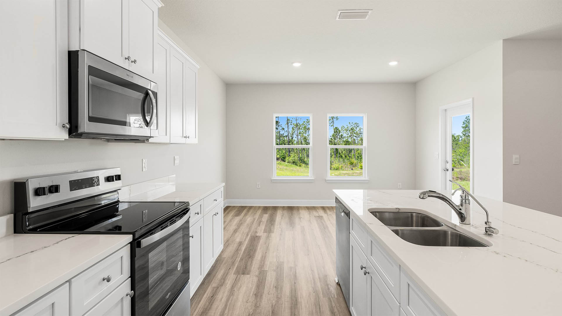 Open kitchen with island and quartz countertops and white cabinets and stainless-steel appliances and dining area with two windows and back door.
