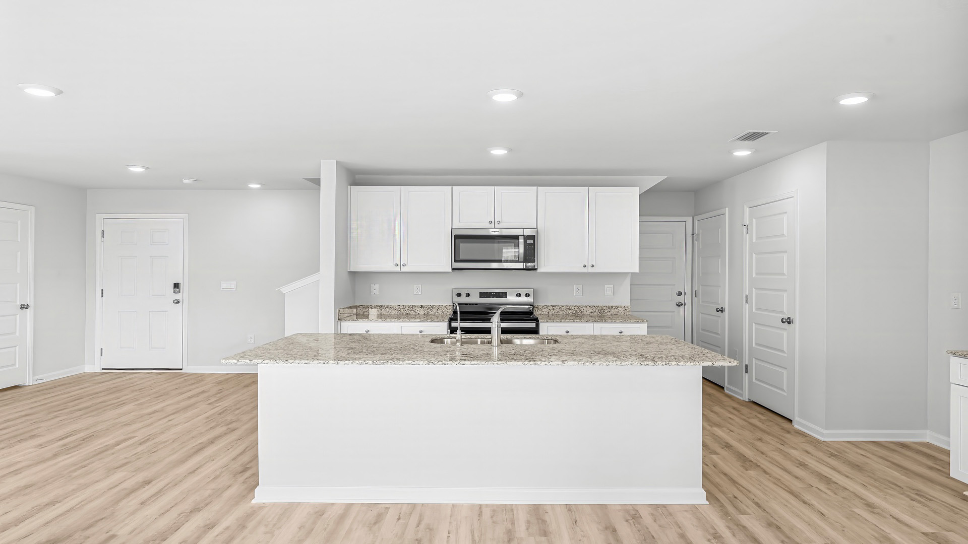 Kitchen with island and granite countertops and white cabinetry and stainless-steel appliances.