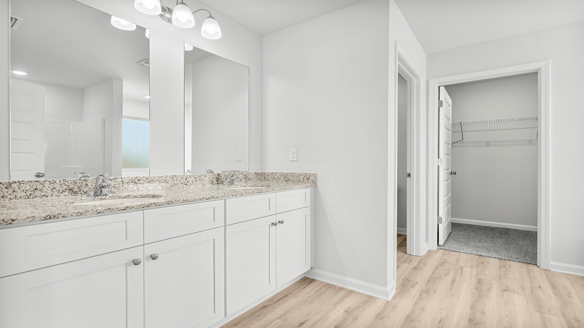 Primary bathroom with double vanity granite countertops and closet entrance.