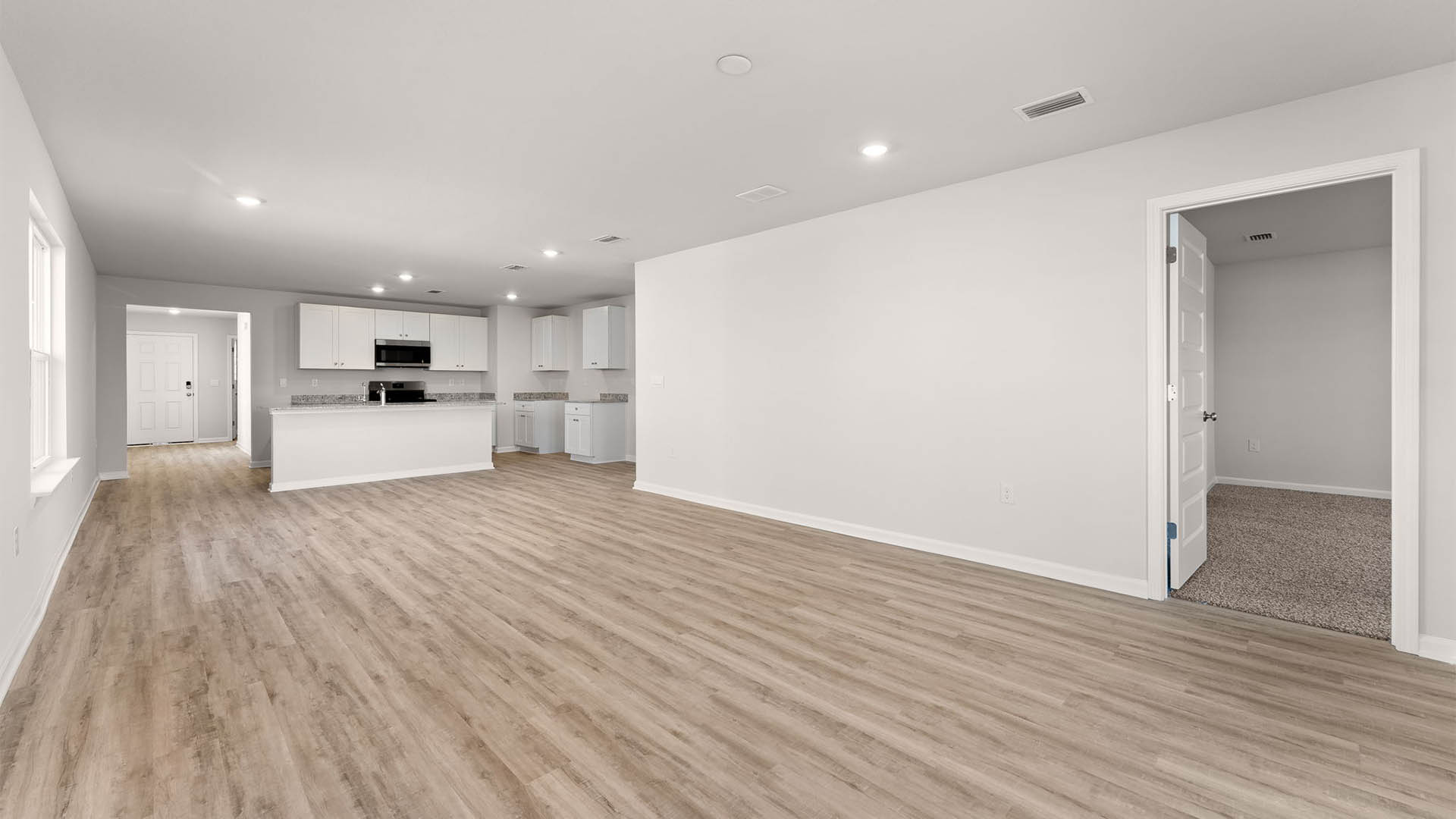 Open living room with primary bedroom entrance and kitchen view.