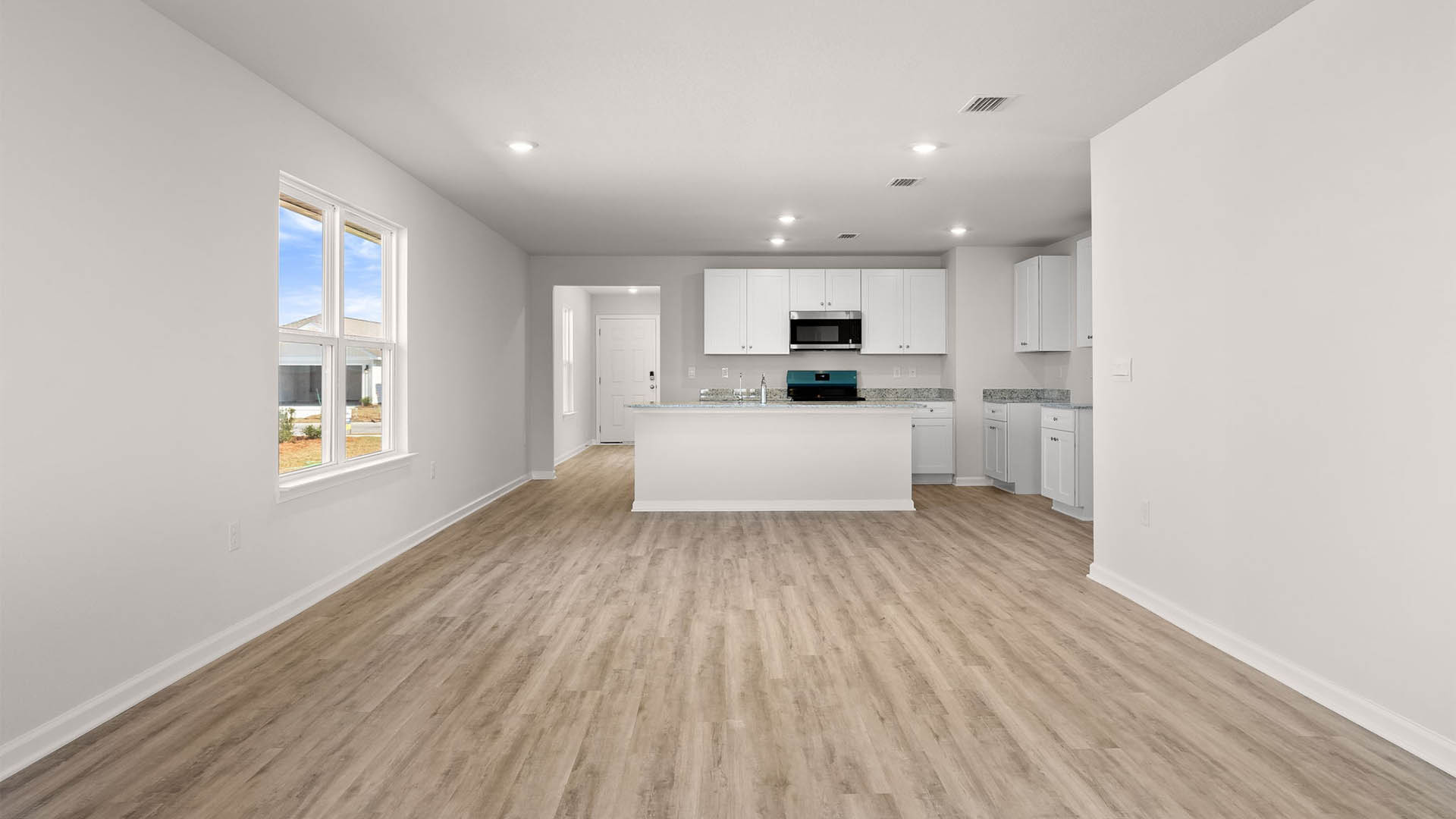Open living room with windows and kitchen view.