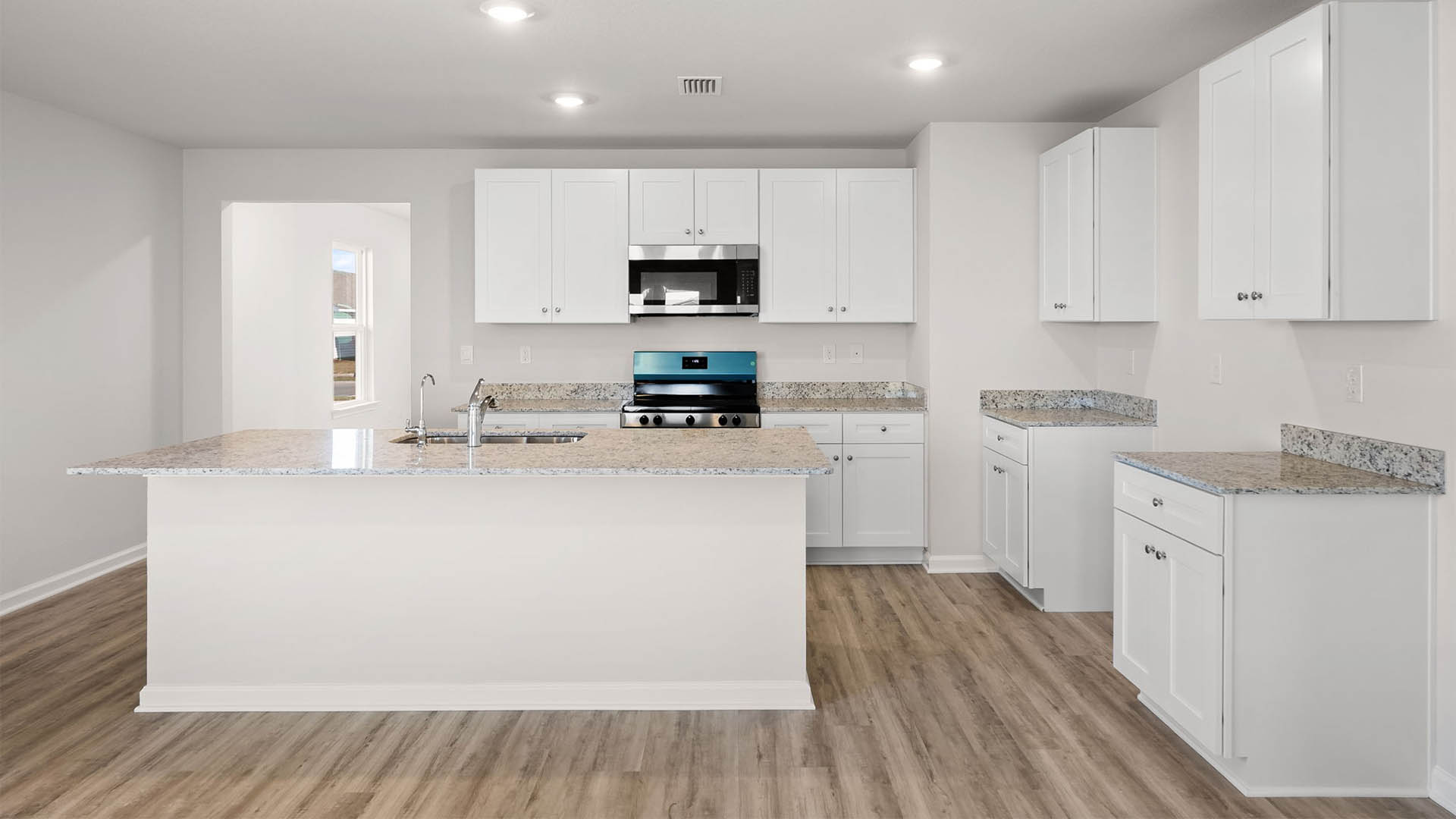 Kitchen with island with granite countertops and stainless-steel appliances and white cabinets.