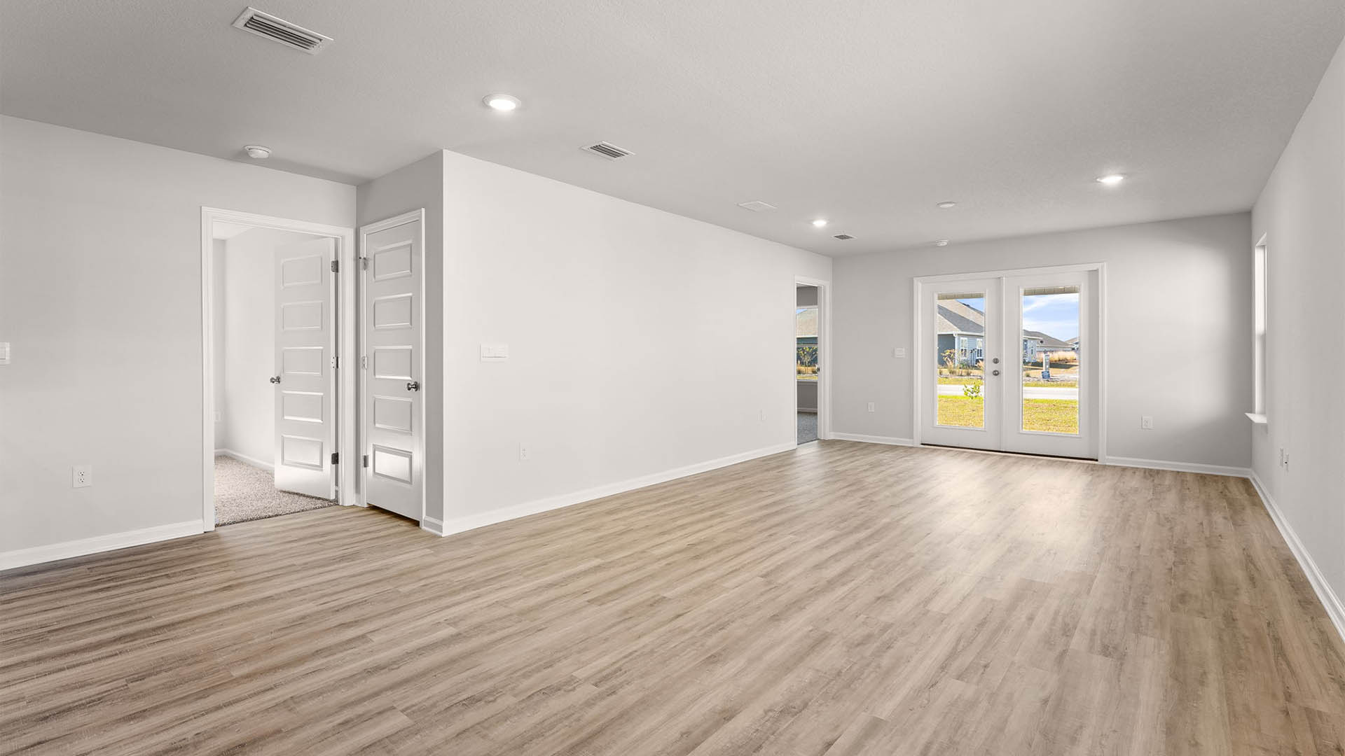 Open living room with dual back doors and primary bedroom entrance and window and bedroom entrances.