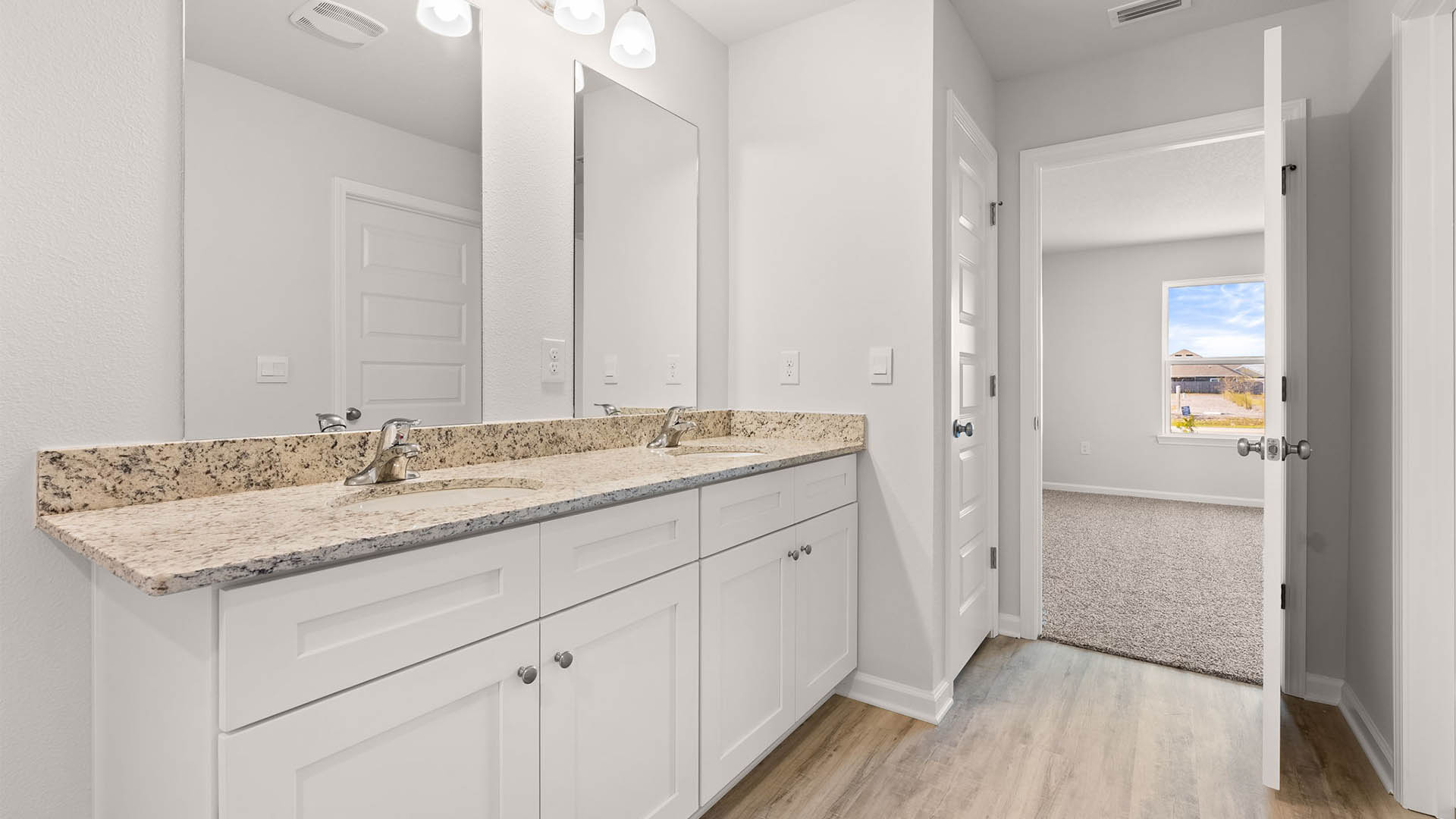 Primary bathroom with double vanity granite countertops and closet and primary bedroom entrance.