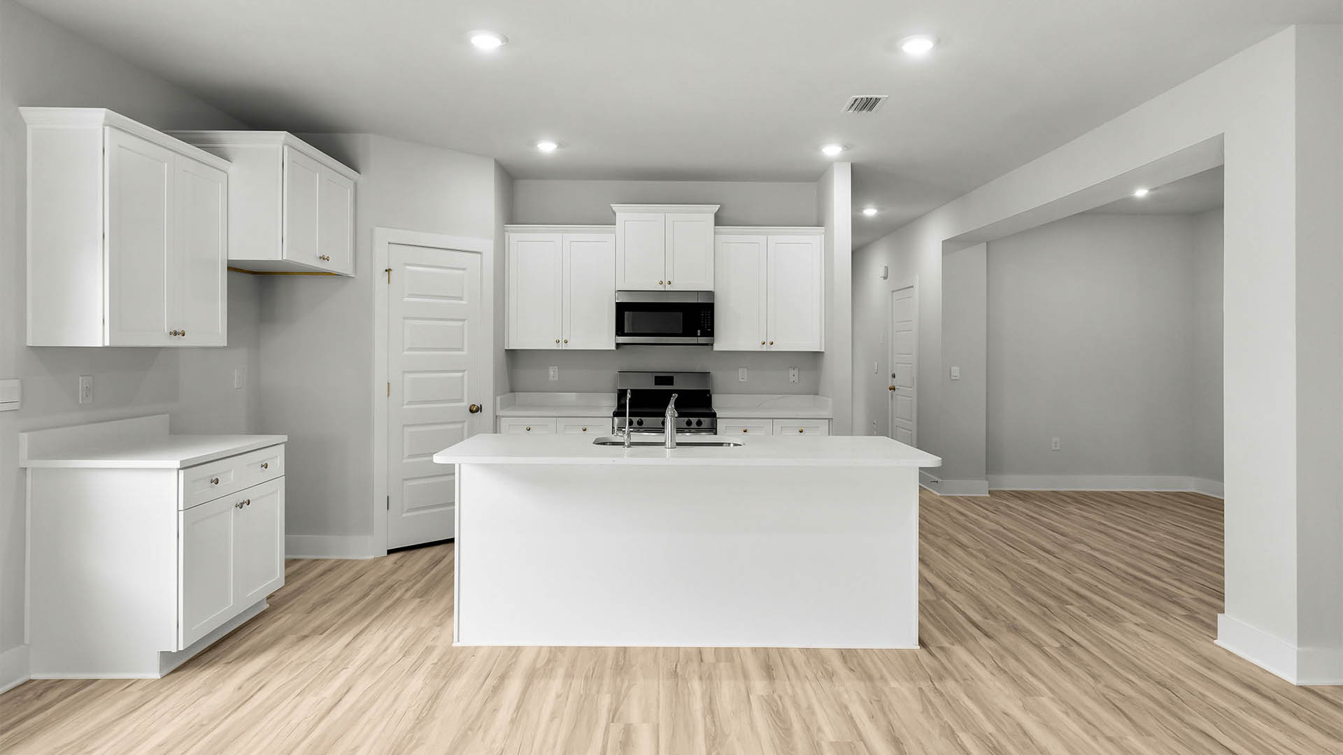 Kitchen with quartz countertops and white cabinetry and island and stainless-steel appliances and pantry.