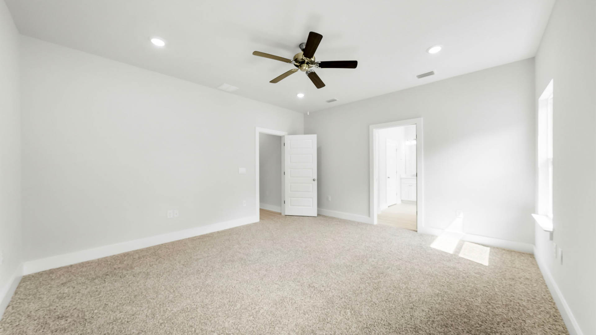 Primary bedroom with carpet flooring and ceiling fan and bathroom entrance.