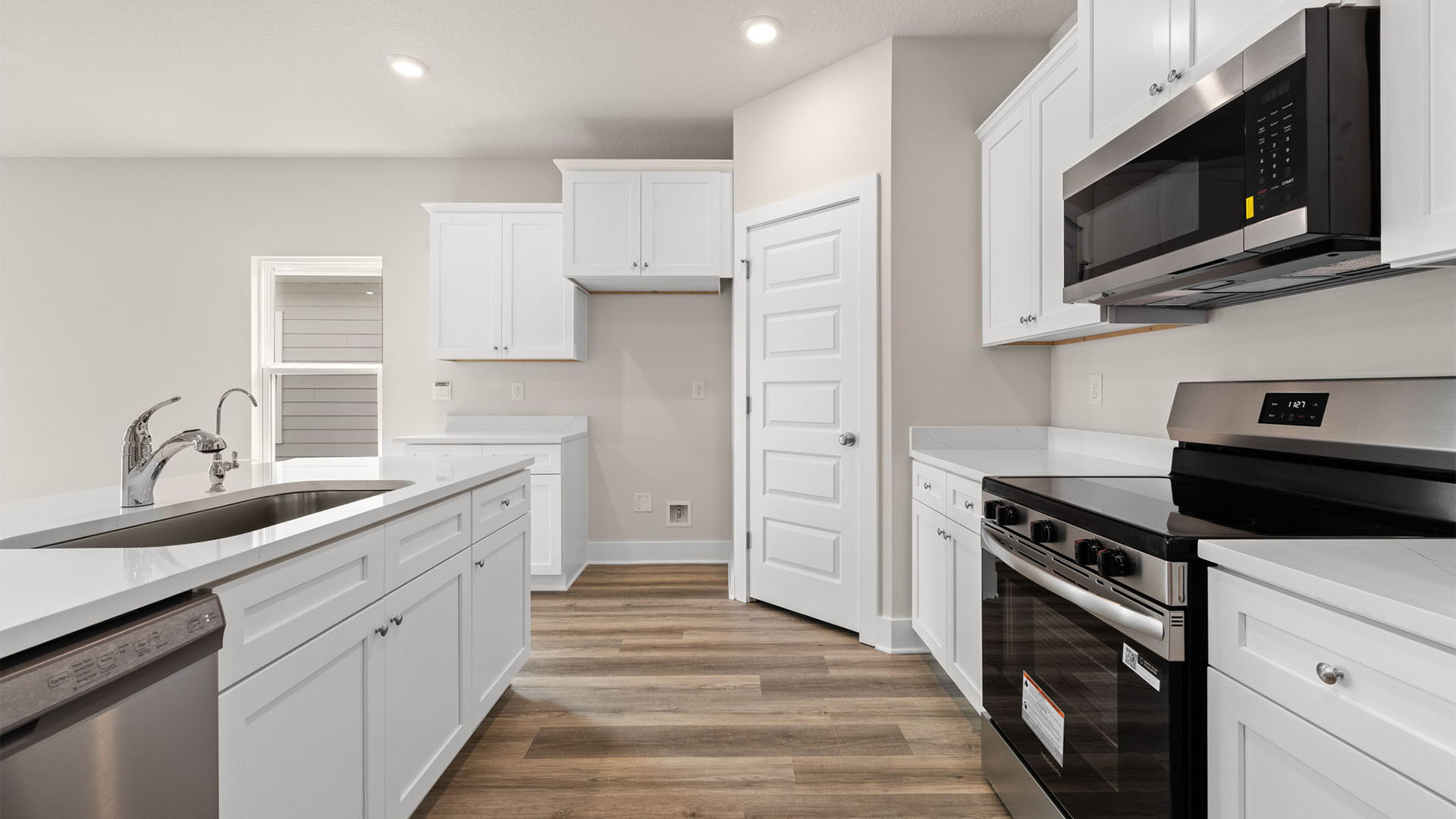 Kitchen with quartz countertops and white cabinetry and island and stainless-steel appliances and pantry.