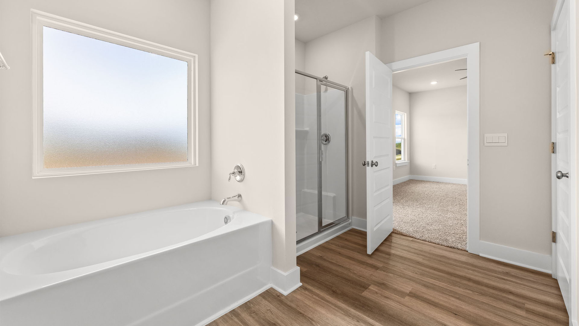 Primary bathroom with glass shower doors and tub with window.