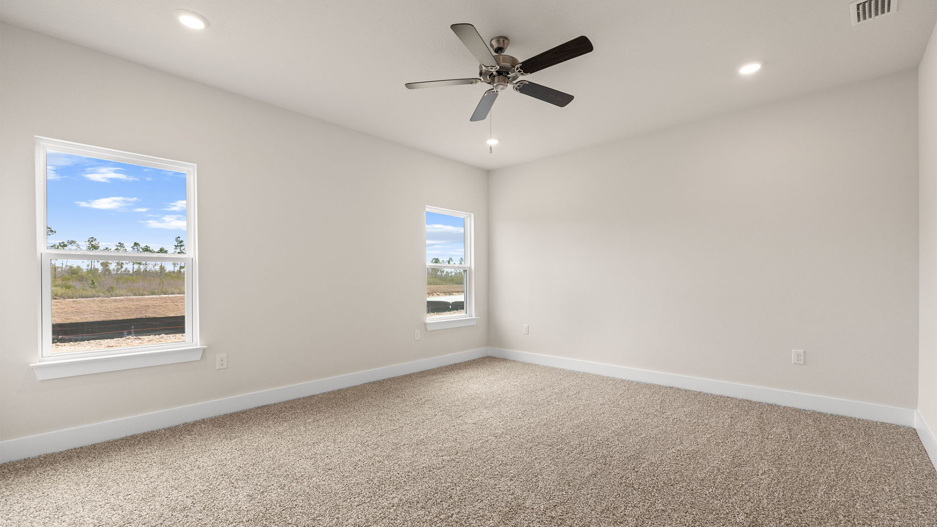 Primary bedroom with carpet flooring and ceiling fan and two windows.